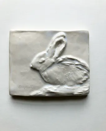 Relief sculpture of a resting rabbit, showcasing fine details and textures on a smooth, rectangular surface. Ideal for art or nature-themed content.