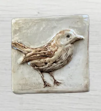 Ceramic tile featuring a detailed relief of a bird, showcasing its expressive features and textures, highlighting craftsmanship in decorative art.