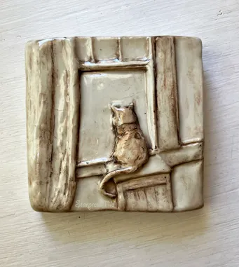 Ceramic tile depicting a cat sitting on a windowsill, gazing outside. The textured design mimics wooden panels, adding warmth and charm.