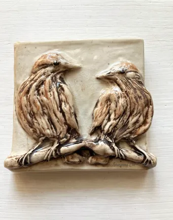 Two intricately sculpted birds sitting on a branch, crafted in ceramic with textured detailing, highlighting their natural forms.