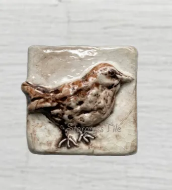 Ceramic tile featuring a raised design of a stylized bird in earthy tones, highlighting craftsmanship and nature-inspired art.