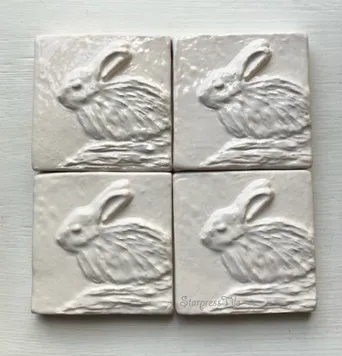 Four textured ceramic tiles featuring raised reliefs of rabbits, showcasing delicate details and a neutral color palette. Ideal for home decor.