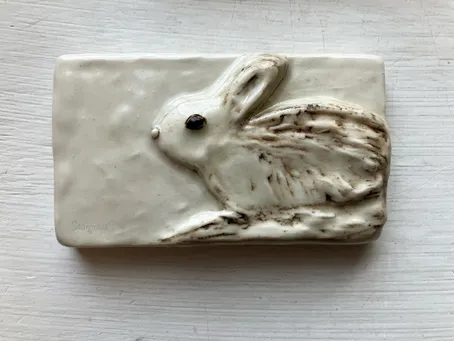 Ceramic plaque featuring a detailed, raised design of a rabbit in profile, showcasing texture and craftsmanship. Ideal for decorative purposes.