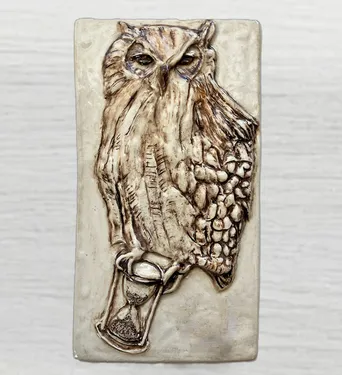 Ceramic wall art depicting an owl holding an hourglass, showcasing intricate textures and details, symbolizing wisdom and the passage of time.