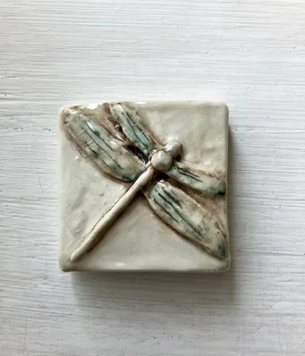 Ceramic tile featuring a detailed, handmade dragonfly design in soft earth tones, showcasing artisanal craftsmanship and nature-inspired decor.