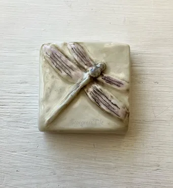 Ceramic tile featuring a textured dragonfly design, emphasizing artistry and craftsmanship, suitable for home decor or artistic display.