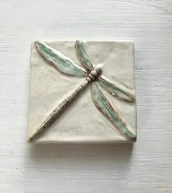 Ceramic tile featuring a textured dragonfly design with subtle blue and brown accents. Ideal for decorative purposes or art displays.