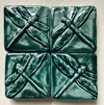 Four ceramic tiles featuring embossed dragonfly designs in a glossy dark green finish. The artwork adds a natural element to home decor.