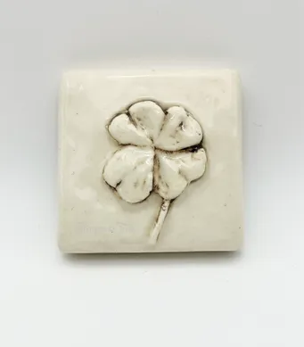 White ceramic tile featuring a raised four-leaf clover design, symbolizing good luck and fortune. Ideal for decorative or inspirational purposes.