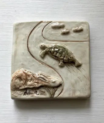 Relief sculpture depicting a tortoise and a rabbit on a winding path, symbolizing perseverance and the classic fable of "The Tortoise and the Hare."